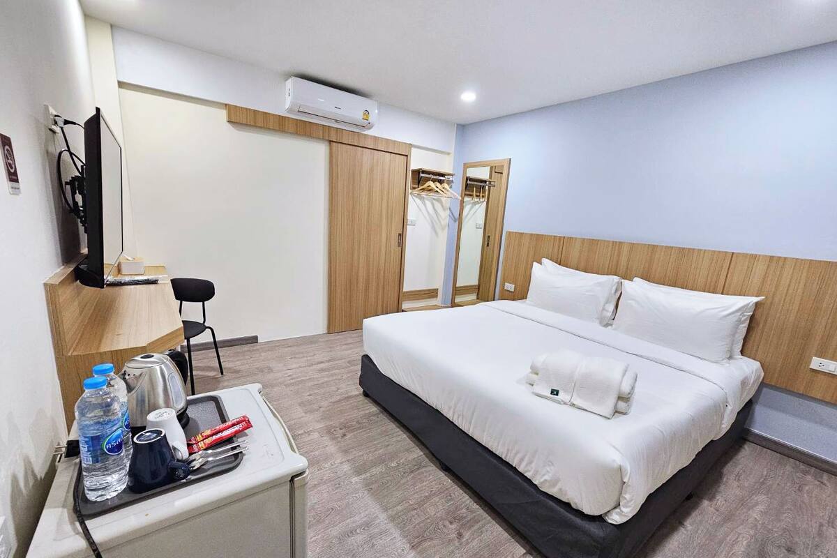 A hotel room with a bed, a desk with a chair, a TV, and a wardrobe.