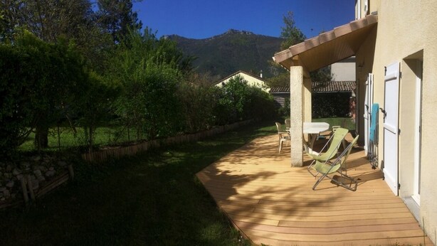 A wooden deck with outdoor furniture, a stone wall, and a mountain in the background.