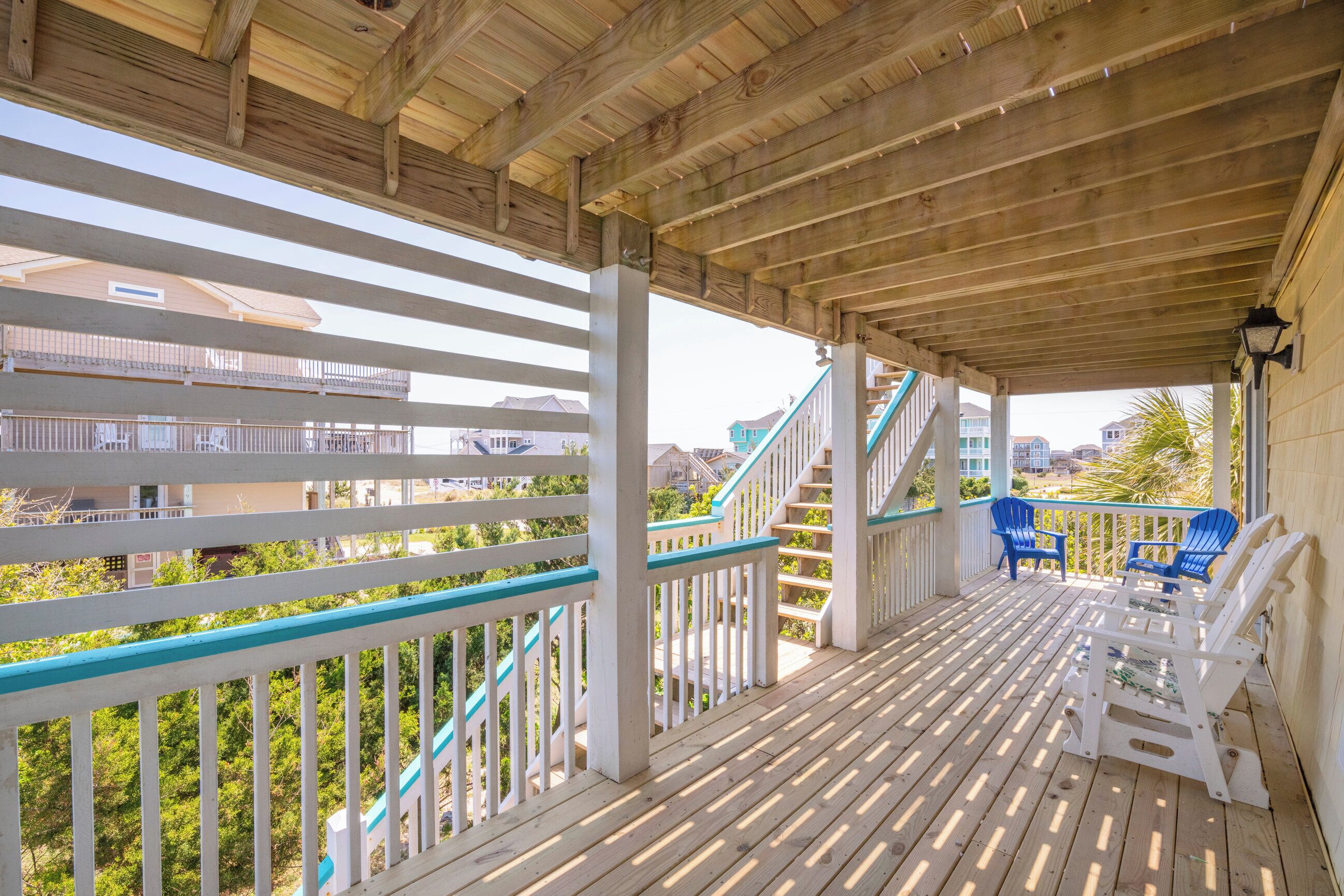 Una terraza de madera con barandillas blancas y detalles azules, con mobiliario exterior y una escalera.