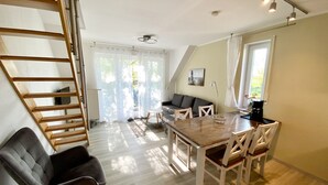 A spacious living area with a wooden dining table, a sofa, and a ladder leading to an upper level.