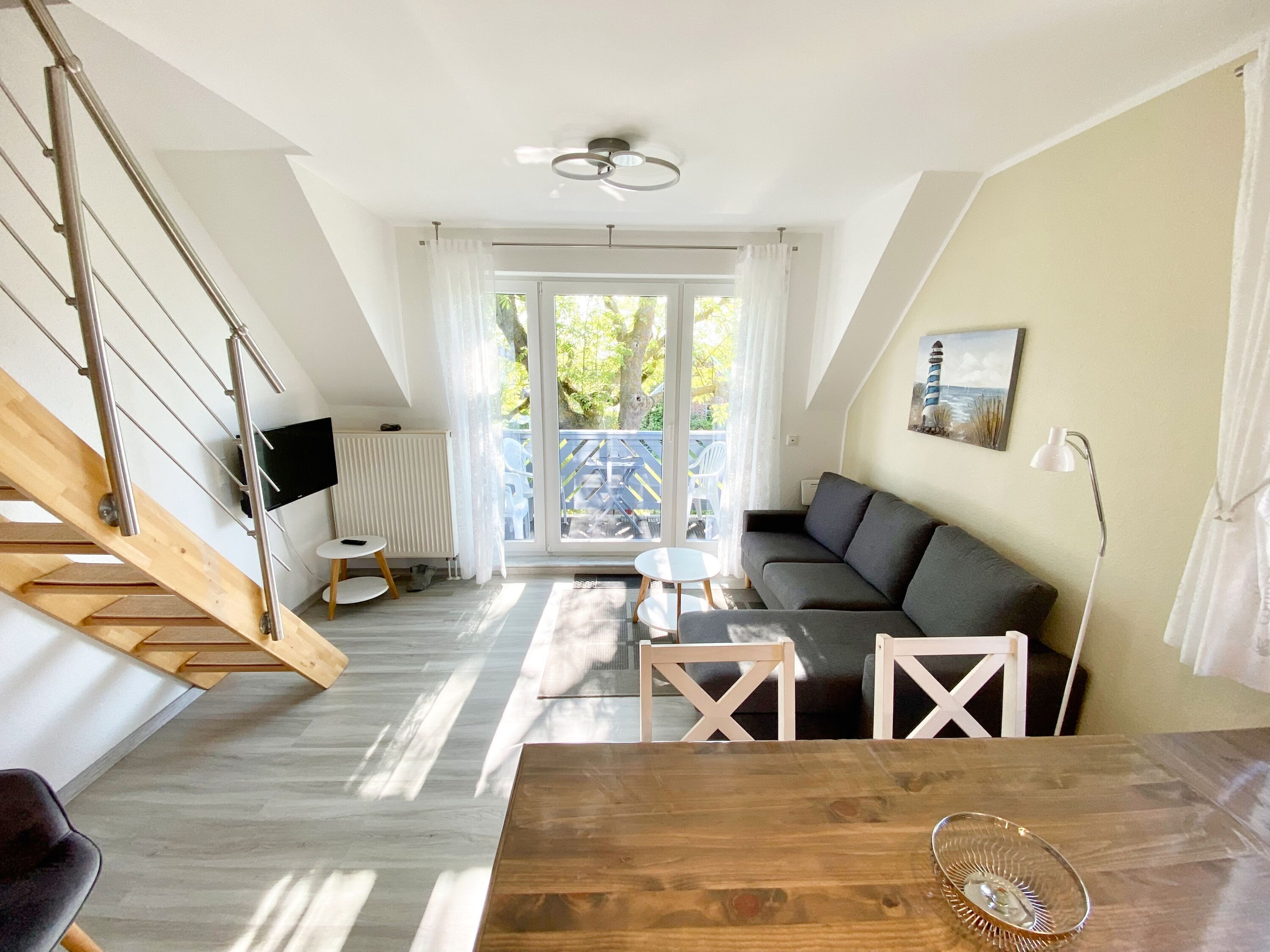 Ein modernes Wohnzimmer mit Treppe, einer Couch, einem Esstisch und Blick ins Freie.