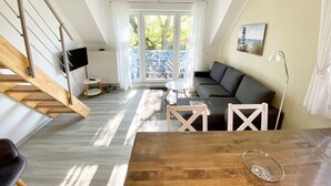 A modern living room with a staircase, a sofa, a dining table, and a view of the outdoors.