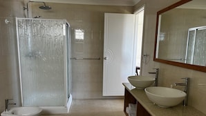 Une salle de bain moderne dotée d’une douche à parois de verre, de deux lavabos, d’un bidet et d’un grand miroir.