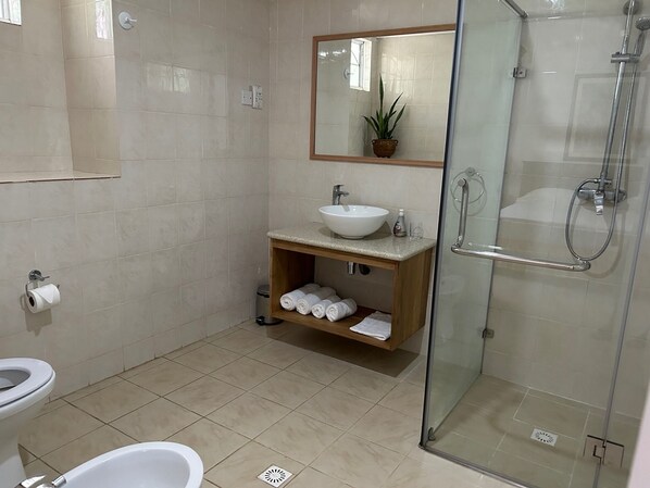 Un baño moderno con ducha de vidrio, lavamanos blanco y retrete.