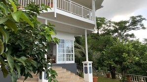 Un bâtiment à deux étages doté d’un balcon, d’un escalier menant à l’entrée et entouré de verdure.