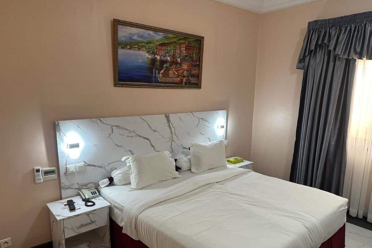 Habitació d'hotel amb un capçal de llit de marbre, un llit amb roba de llit blanca, una taula de nit amb un telèfon i un quadre a la paret.