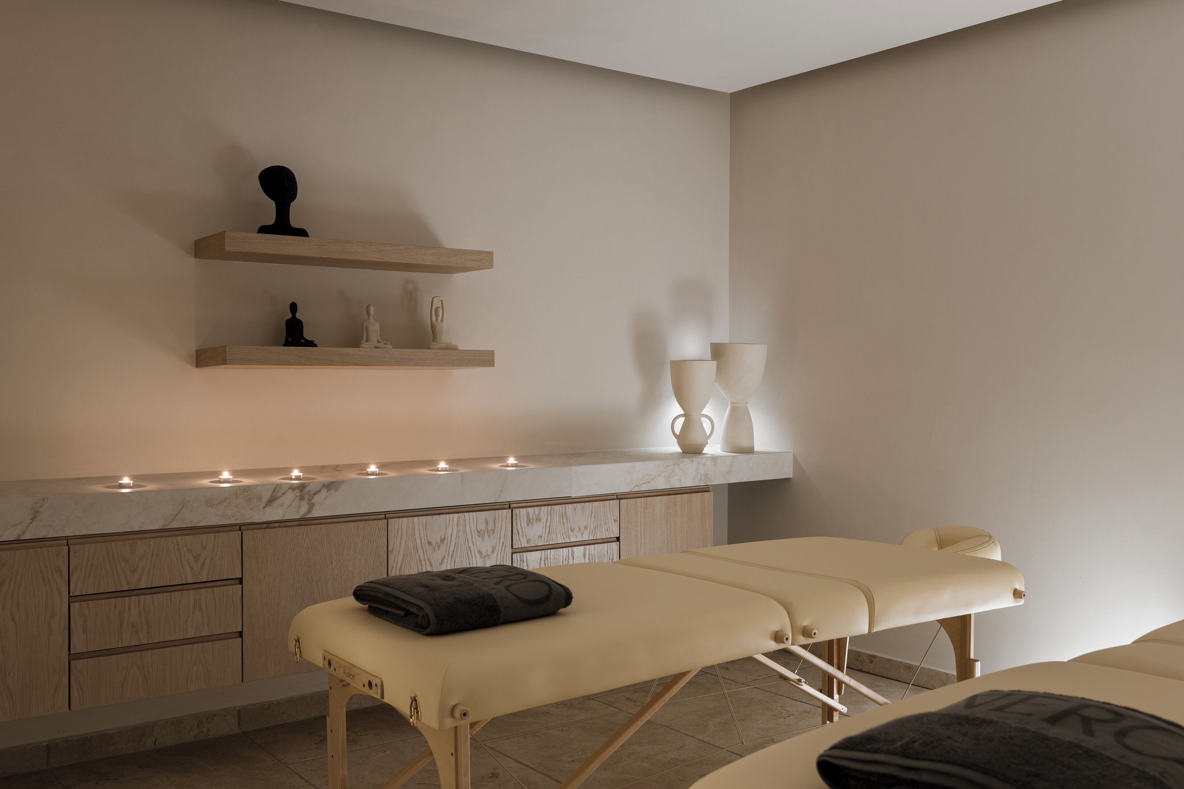Une salle de spa équipée d’une table de massage, de meubles en bois et d’un comptoir en marbre agrémenté de bougies.