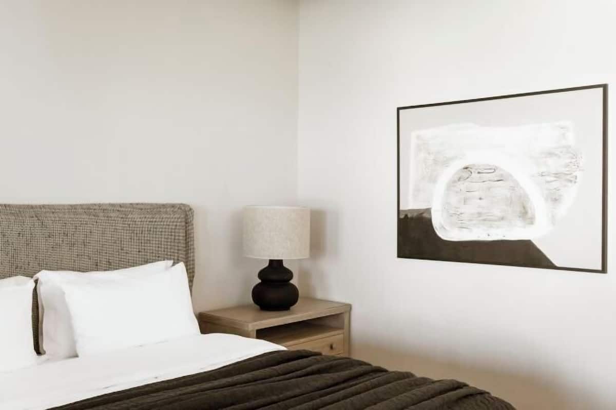 A bedroom with a bed, a nightstand with a lamp, and a framed picture on the wall.