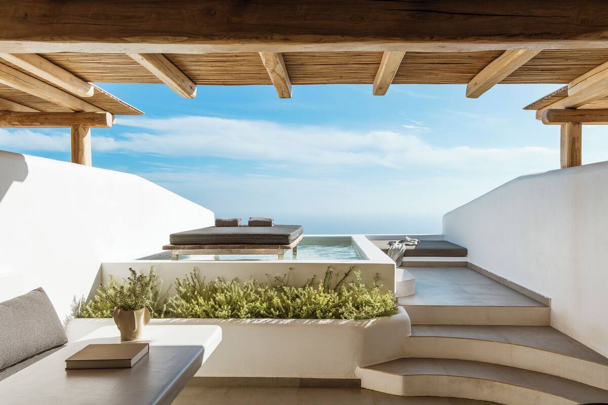A modern outdoor lounge area with a pool, seating, and a view of the ocean.