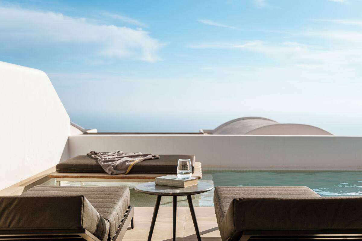 A sunlit outdoor seating area with a pool, a glass of water, and a book on a small table.