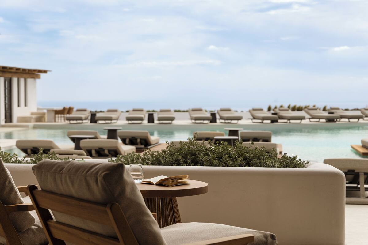 A poolside area with lounge chairs and a table, overlooking a pool and a clear sky.