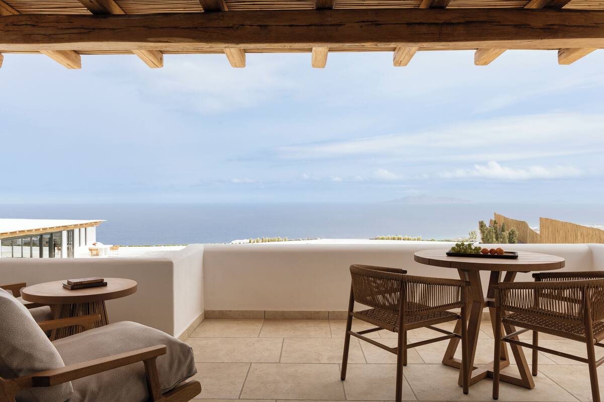 A wooden pergola with a round table and wicker chairs, overlooking a coastal view.