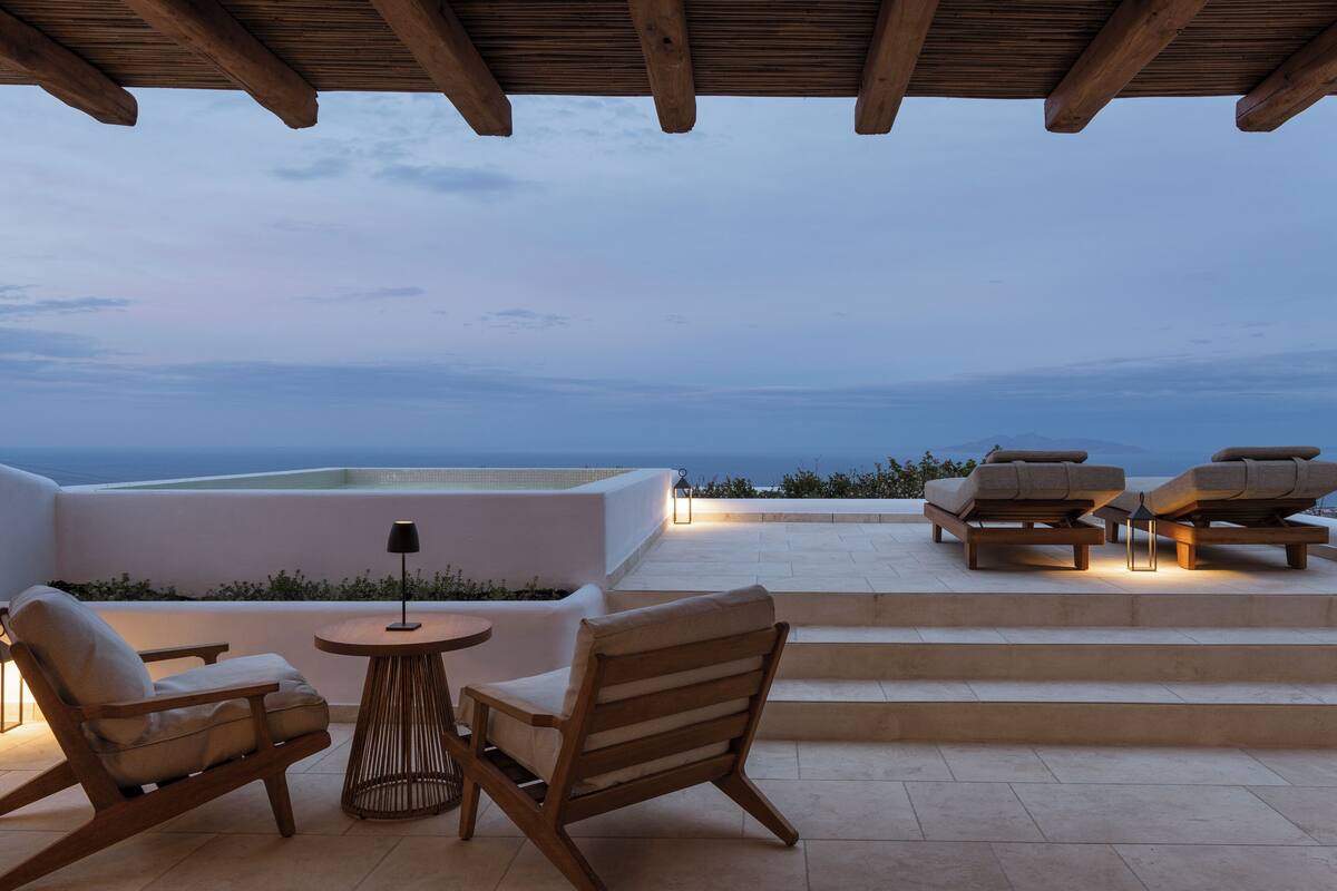 A terrace with outdoor seating, a lamp, and a view of the sea.