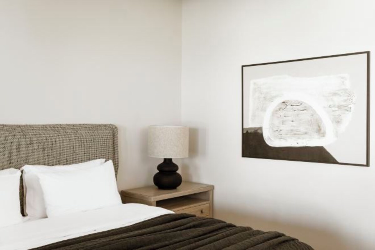 A bedroom with a bed, a nightstand with a lamp, and a framed picture on the wall.