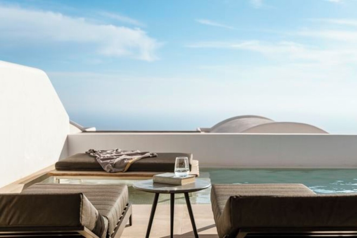 A balcony with a view of the sea, a small round table with a book and glass, and two lounge chairs.