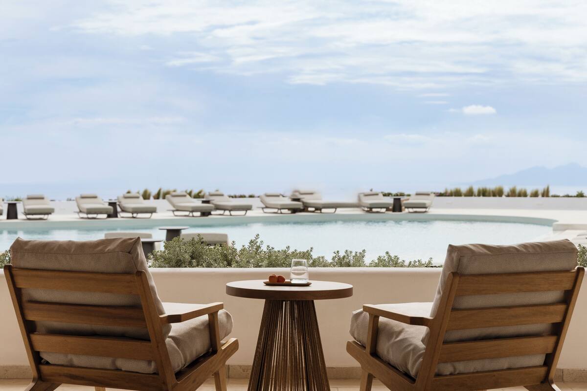 A poolside area with lounge chairs and a table, overlooking a pool and distant mountains.