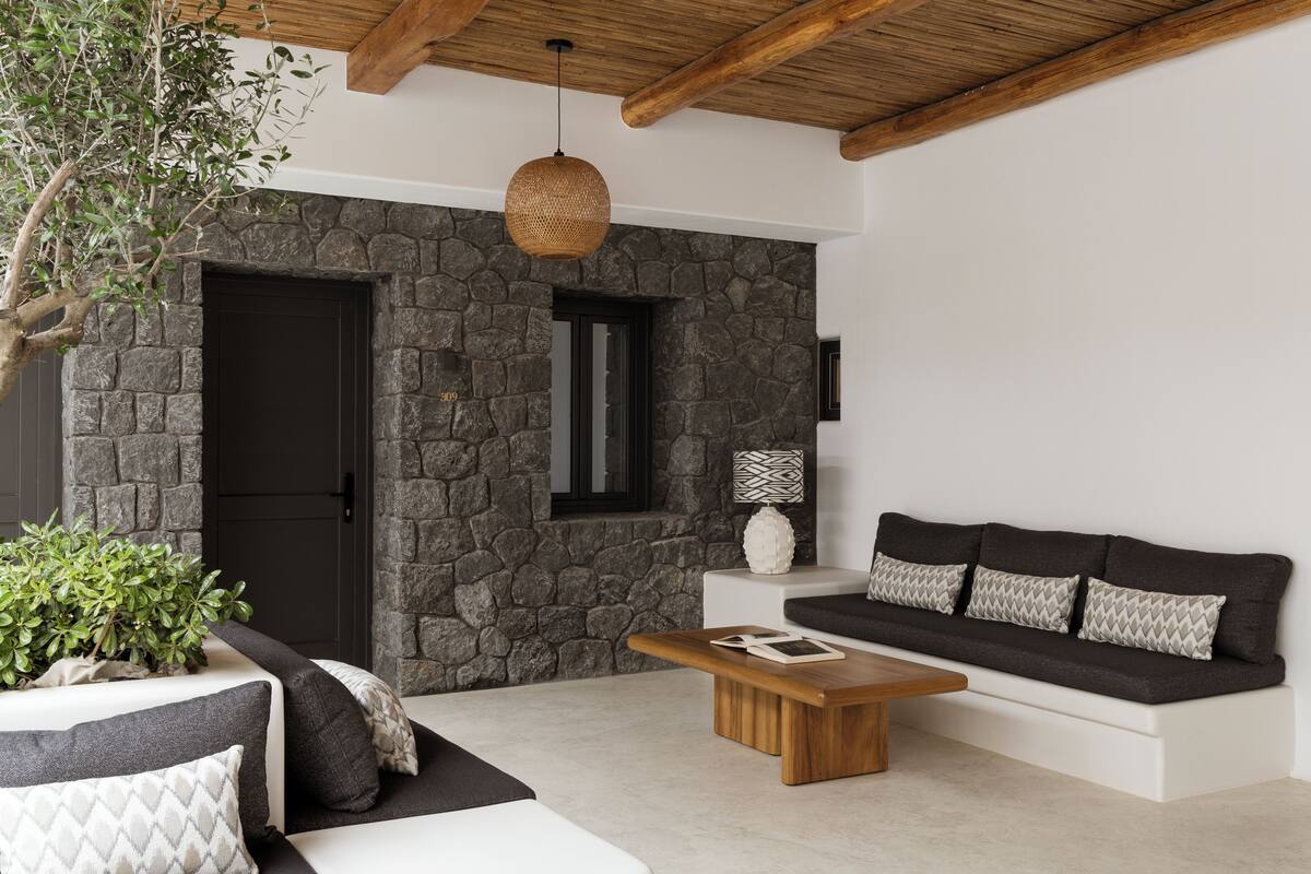 A modern living room with a stone wall, a wooden ceiling, a sofa set, and a coffee table.