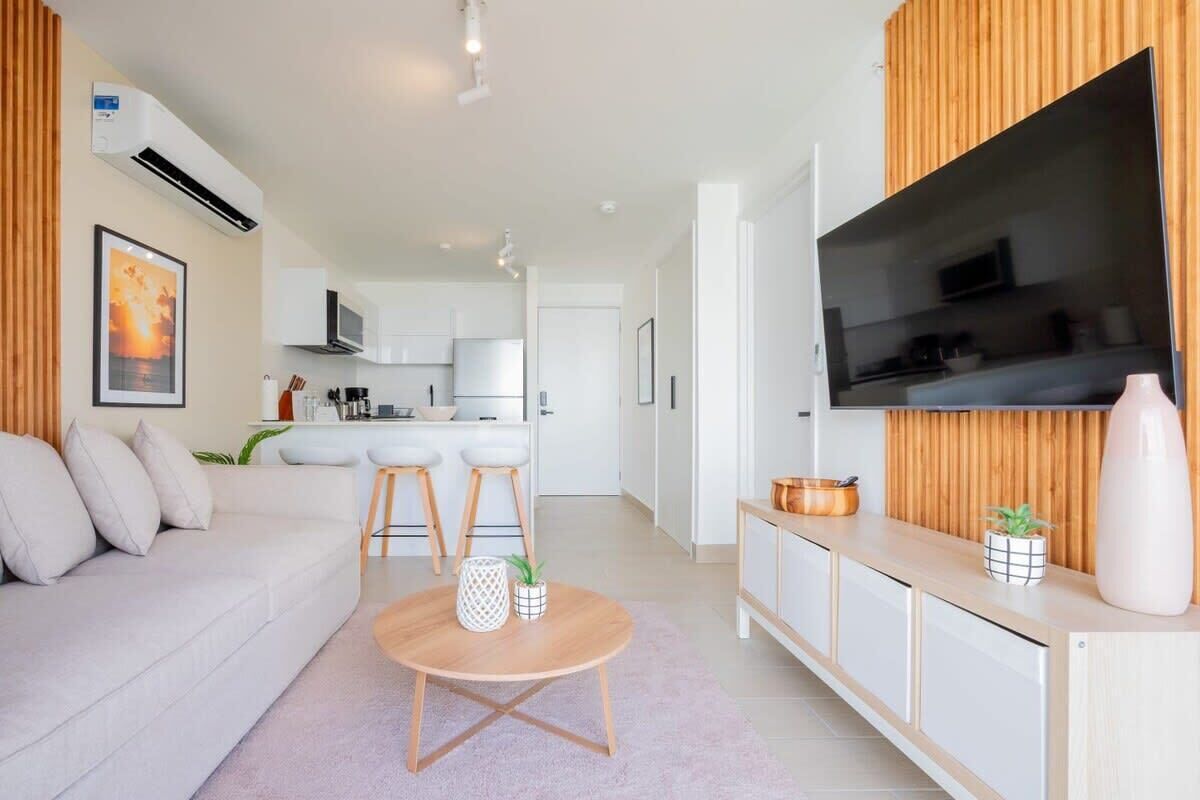 A modern living room with a sofa, a round coffee table, and a TV mounted on a wooden panel.