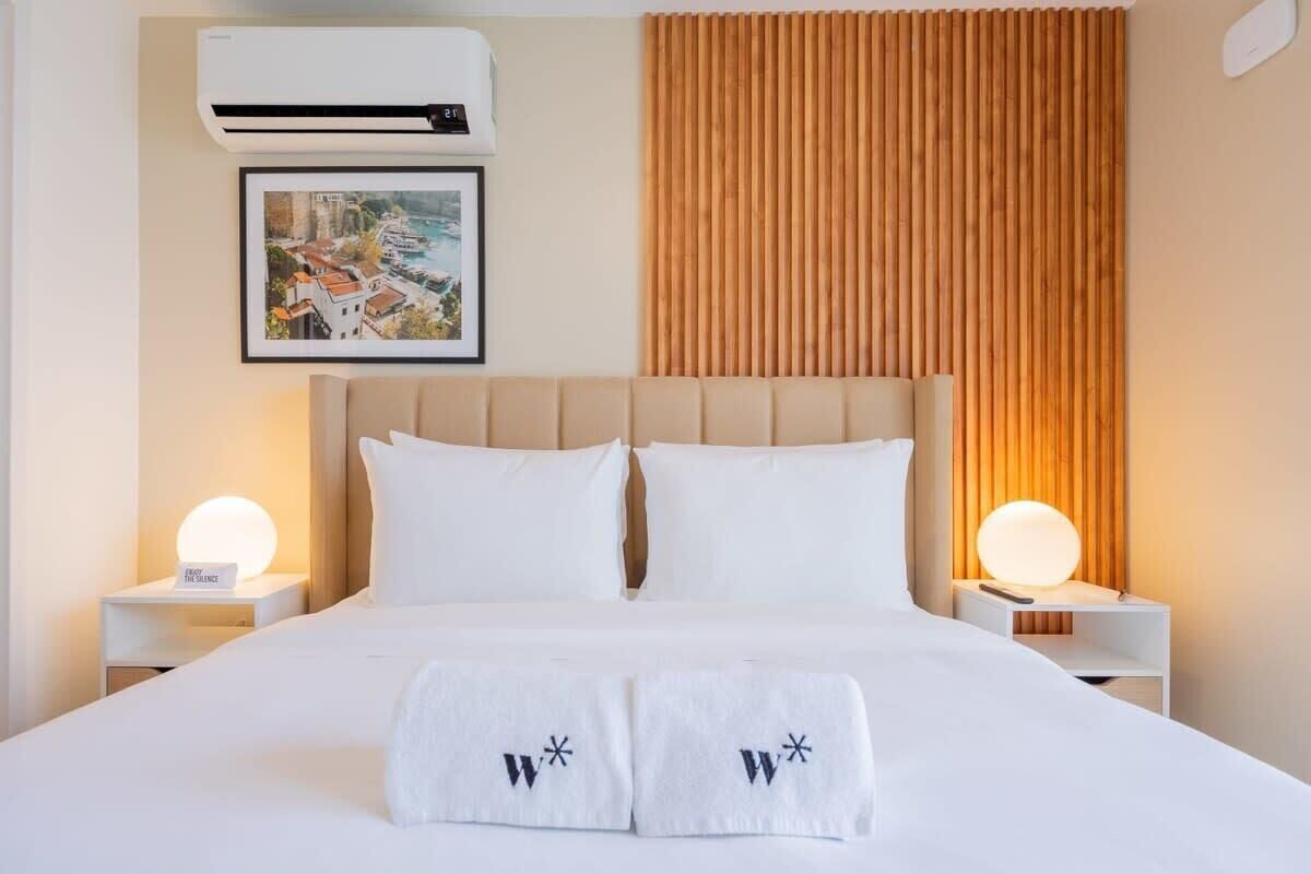 Una habitación de hotel con una cama grande, dos mesitas de noche con lámparas, un cuadro enmarcado en la pared y un panel de madera.