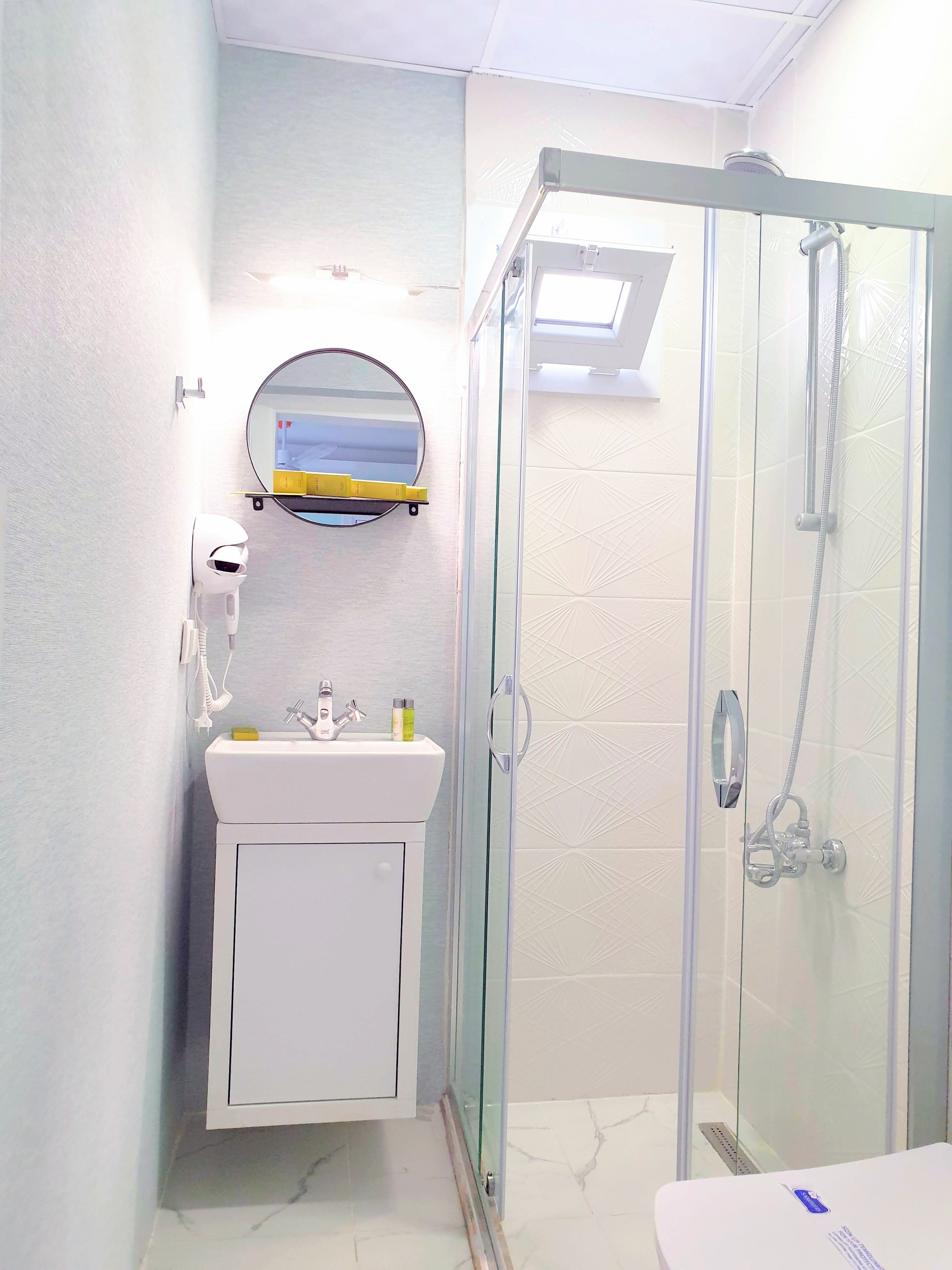 Un baño con ducha envuelta en vidrio, un lavamanos con espejo y un mueble inferior.