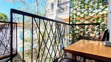 Un balcón con una mesa de madera y un banco acolchado, con vistas a una zona residencial con casas y un árbol.