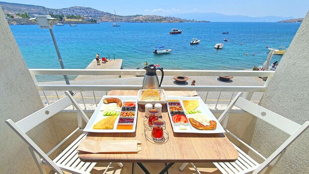Un balcon avec une table préparée pour le petit-déjeuner, donnant sur une étendue d’eau où se trouvent des bateaux.
