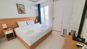 Un lit bien fait, avec du linge de lit blanc, une table de chevet avec une lampe, une armoire et un tableau accroché au mur.