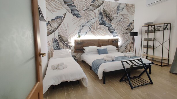 Un dormitorio con dos camas individuales, un banco, un armario y un gran diseño de hojas en la pared.