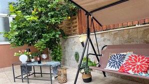 Un patio con una hamaca, una mesa con un florero y una botella de vino, y una planta en maceta.