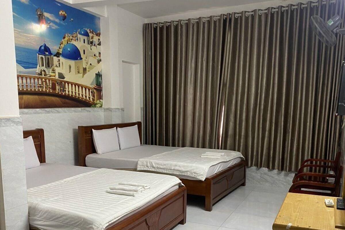 A hotel room with two wooden beds, a desk, and a large window with curtains.