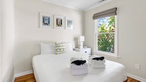 A neatly arranged bedroom with a bed, bedside tables, a window with a view, and framed pictures on the wall. - Crescent Cottage | Walk to Republic + Prohibition (Charleston)