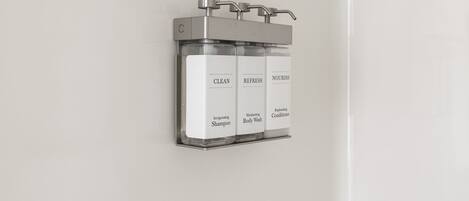 A wall-mounted dispenser with three bottles labeled "CLEAN," "REFRESH," and "NOURISH," containing "Invigorating Shampoo," "Moisturizing Body Wash," and "Replenishing Conditioner."