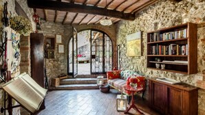 A rustic room with a stone wall, wooden beams, a bookshelf, a sofa, and a large open door leading outside. - RIPOSTENA COUNTRY HOUSE The Shed (Casole)