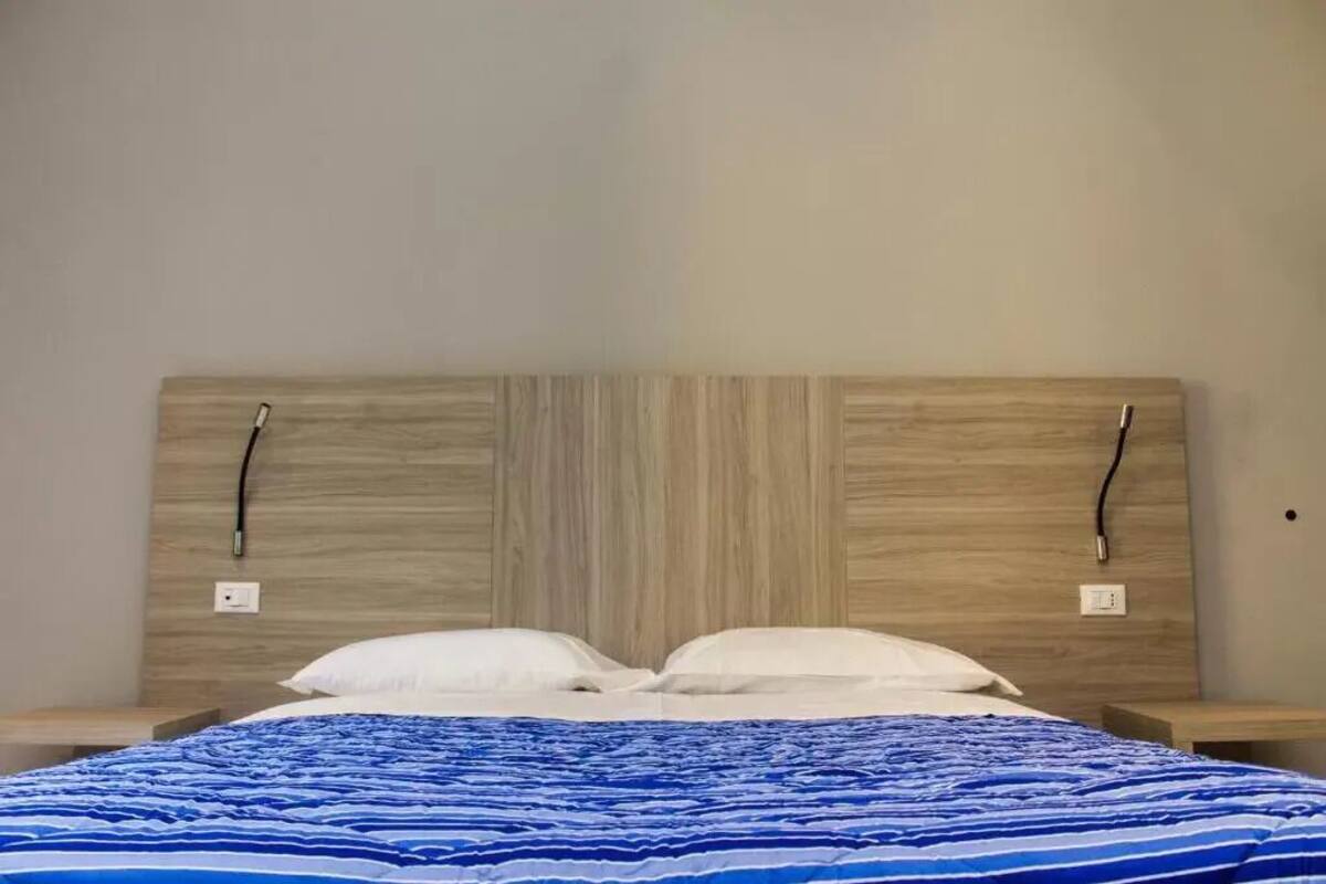 Una cama con cabecera de madera, almohadas blancas y colcha a rayas azules.