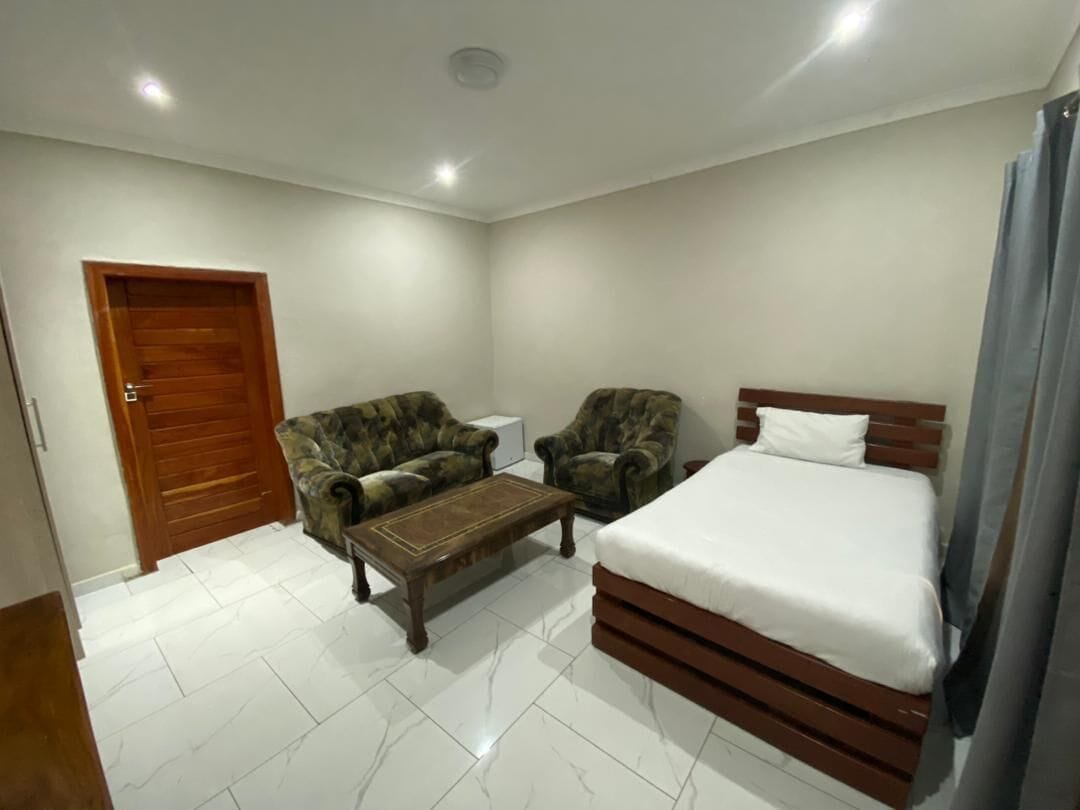 A room with a bed, two armchairs, a small table, and a wooden door.