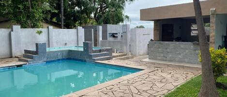 Uma piscina com deck de pedra, rodeada por um pequeno muro e área de jardim.