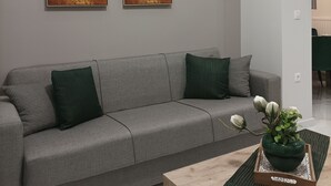 A modern living room with a grey sofa, two abstract paintings, and a wooden coffee table with a green plant. - Atelier Deluxe Apt Must (Thessaloniki)