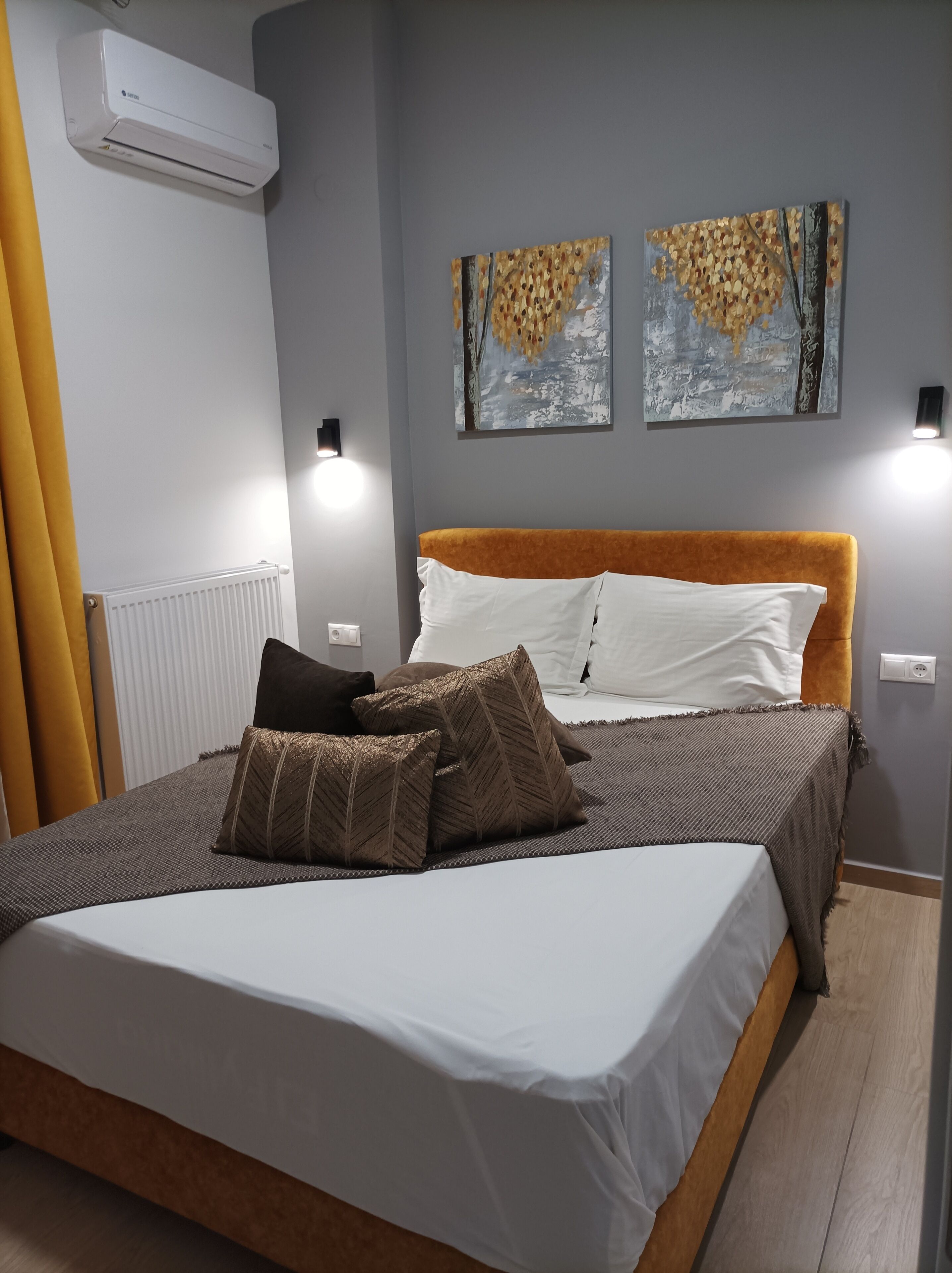 Un dormitorio con cama, dos luces empotradas, aire acondicionado y dos cuadros abstractos.