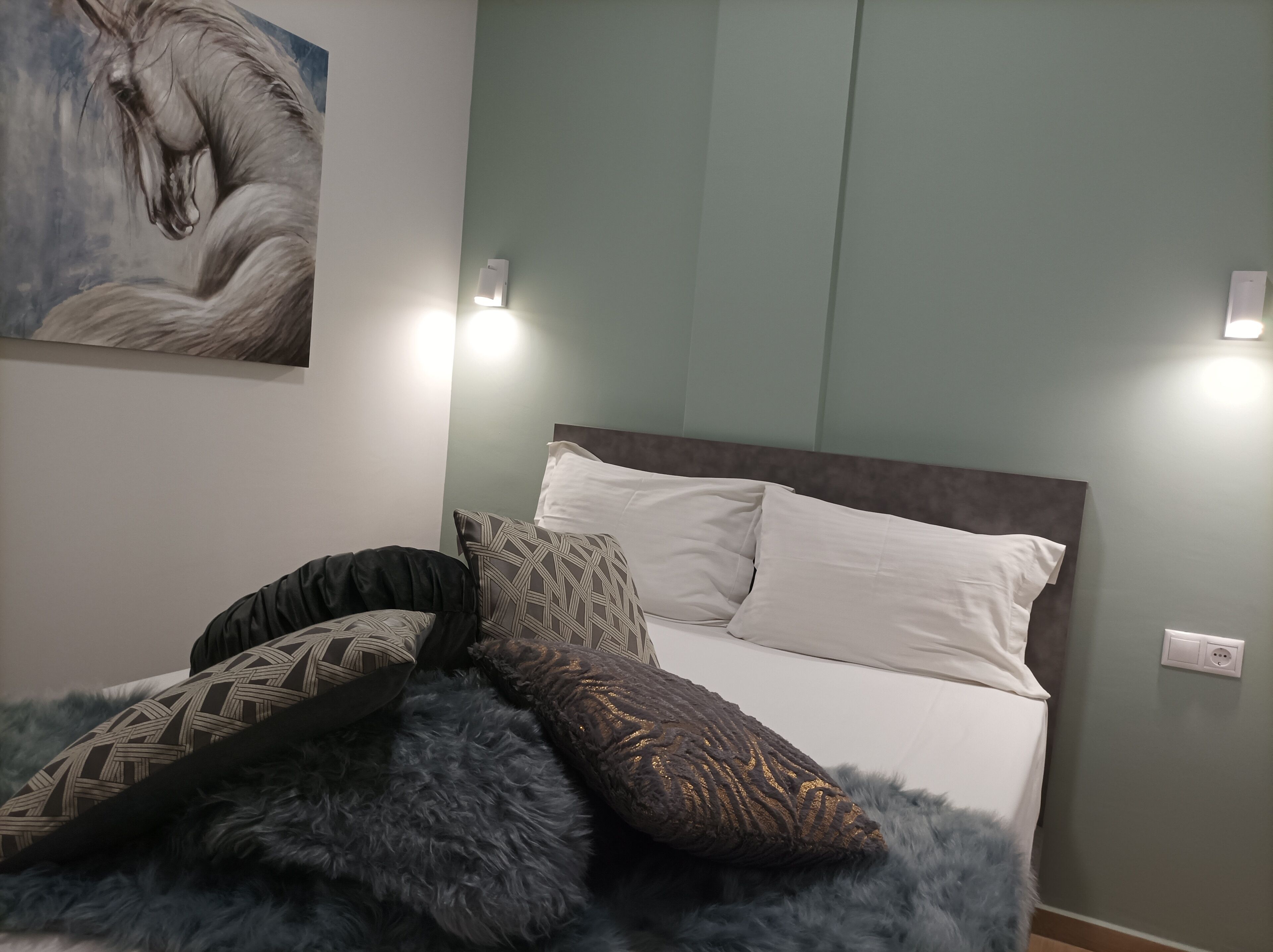 Un dormitorio con cama, almohadas, una lámpara de pared y un cuadro.