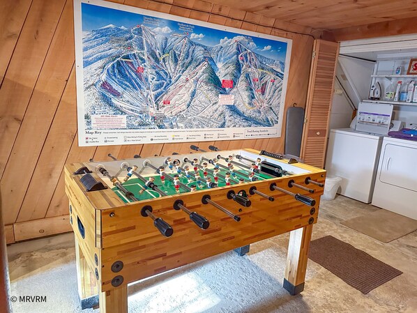 Habitación con piso de madera, mesa de fútbol de mesa y un mapa grande de una estación de esquí en la pared.