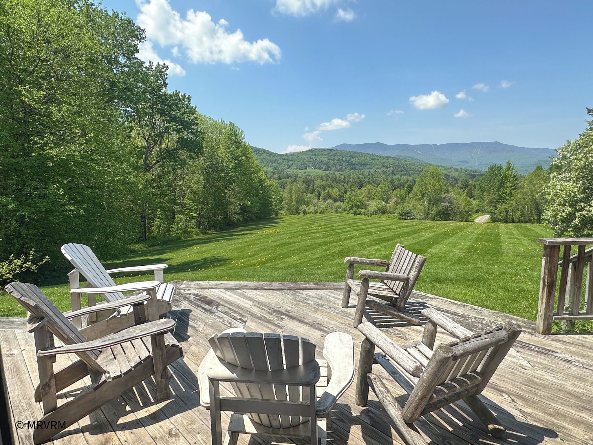 Eine Holzterrasse mit Adirondack-Stühlen, mit Blick auf eine Wiese und ferne Berge.