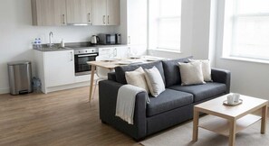 A modern kitchen with a dining area, a gray sofa, and a small table with cups. - Comfortable 1BR Apartment in Manchester (Manchester)