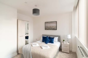A bedroom with a bed, bedside table, lamp, and a window. - Comfortable 1BR Apartment in Manchester (Manchester)