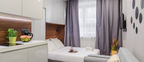 A modern hotel room with a kitchenette, a bed with a tray of breakfast, a sofa, and a wall with decorative mirrors.