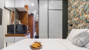 Habitación de hotel moderna con cama, televisor y bandeja de desayuno con croissants y té.