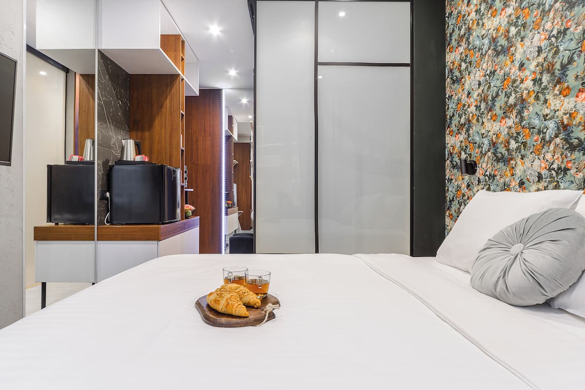 A modern hotel room with a bed, a TV, and a breakfast tray with croissants and tea.