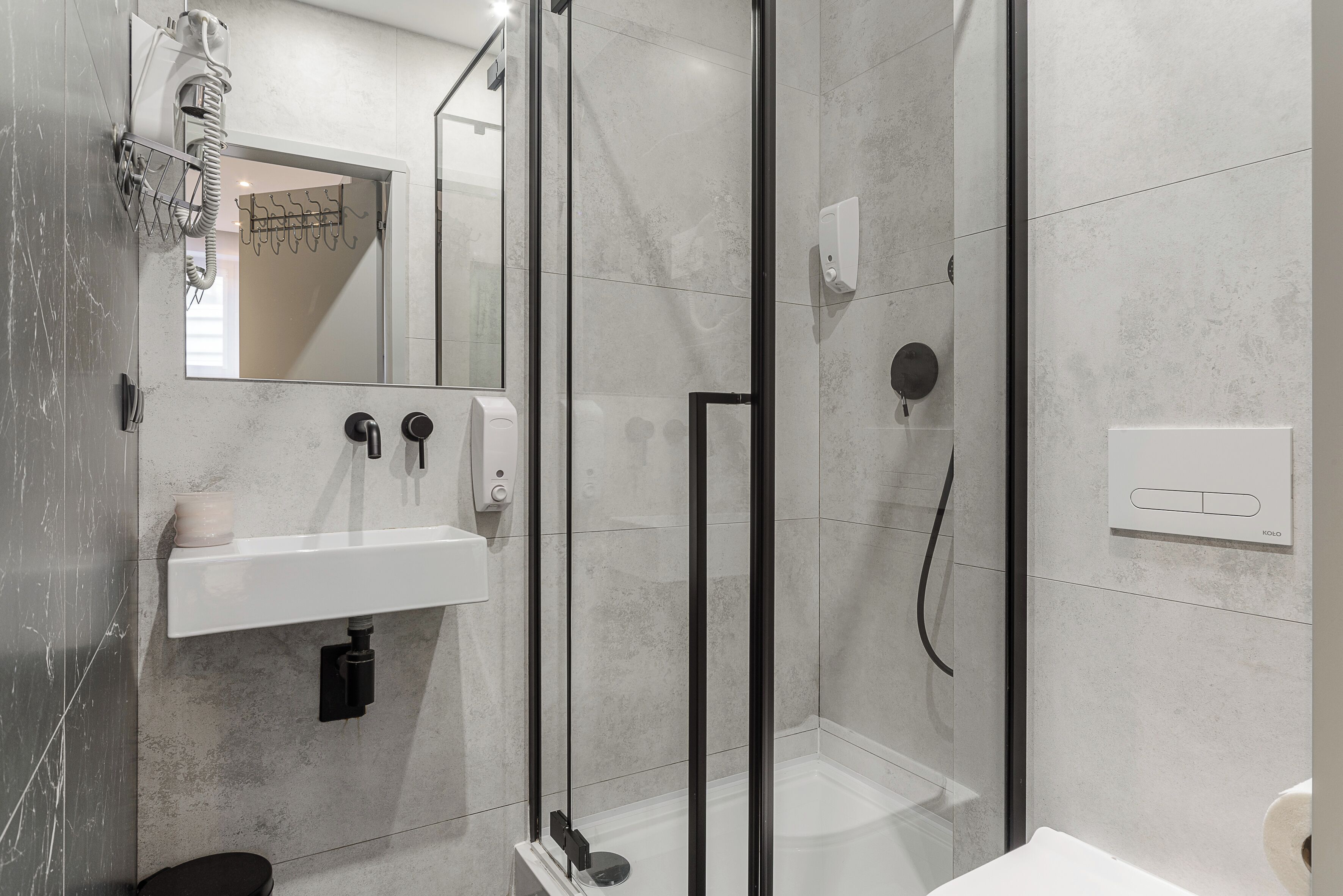 Un baño moderno con ducha envuelta en vidrio, un lavamanos con dispensador de jabón y un espejo sobre el lavamanos.