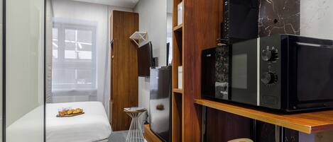 Una kitchenette compacta con microondas, un refrigerador pequeño y un estante de madera con frutas.