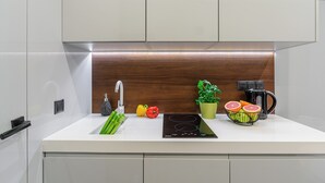 Una cocina moderna con armarios blancos, un protector contra salpicaduras de madera, un lavamanos, una estufa y una cafetera.
