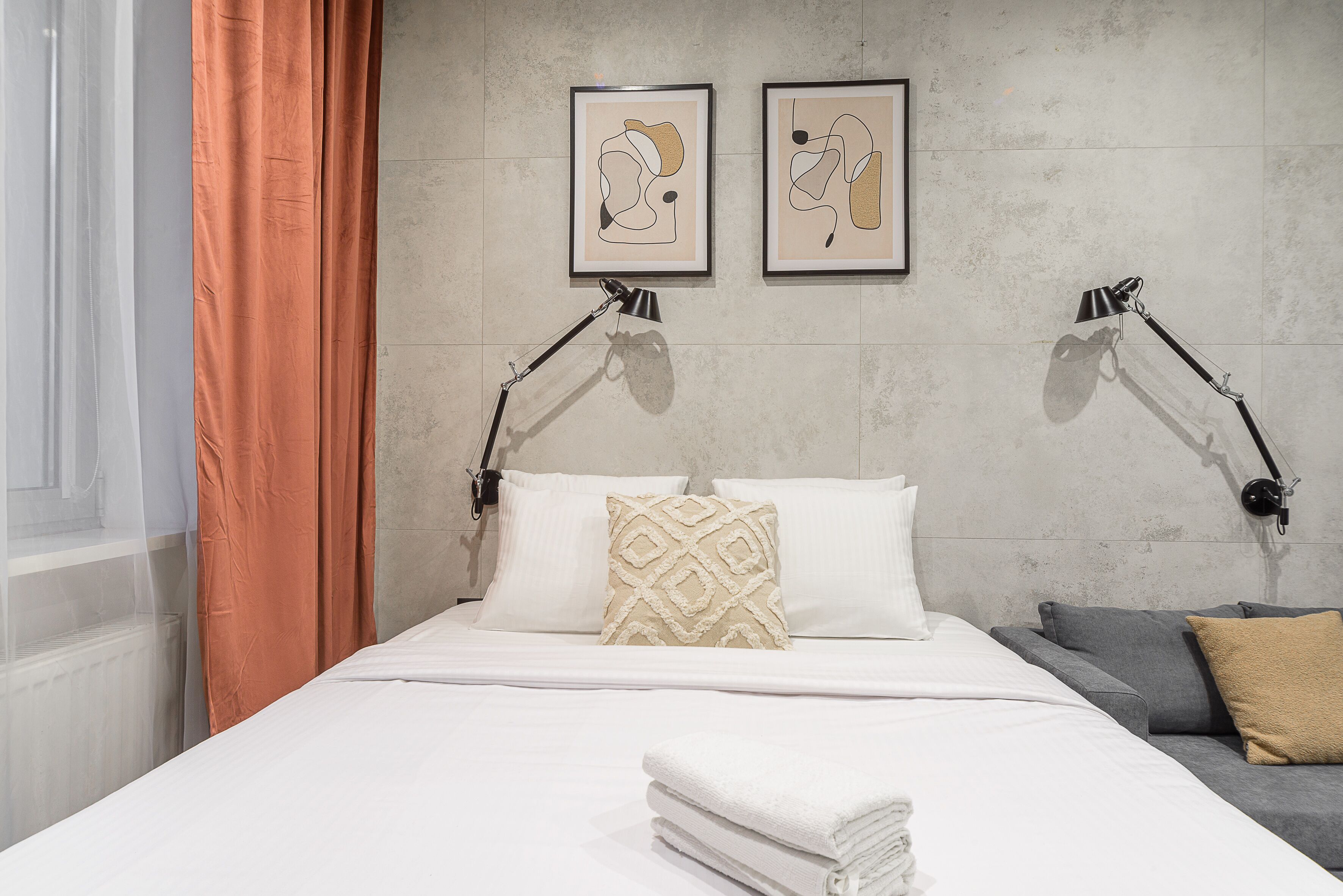 Un lit bien fait, avec du linge de lit blanc, un coussin à motifs beige et deux œuvres d’art abstraites encadrées accrochées au mur.